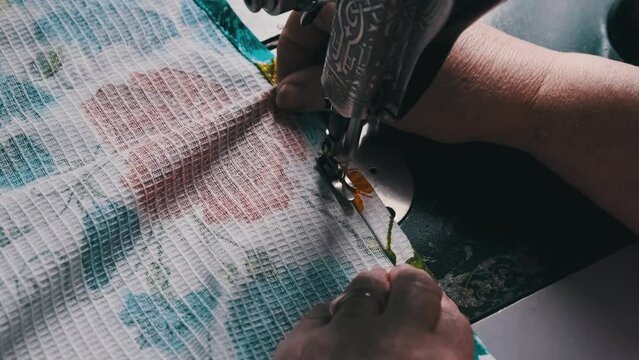 An aged seamstress sews at a traditional sewing machine at home in slow motion. Close-up of aged female hands working at a retro sewing machine. The needle quickly moves up and down. Lifestyle, hobby