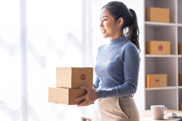 Portrait of Starting Asian female small businesses owners SME entrepreneur working at Laptop in home Warehouse, online marketing, packing boxes, SME sellers, concept, e-commerce team, online sales.
