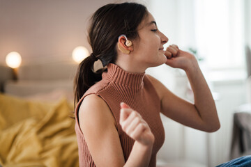 Teenage girl with hearing aid listening music in her room. - obrazy, fototapety, plakaty
