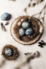 Easter painted eggs in a nest with willow branches on a light stone background. Flat lay