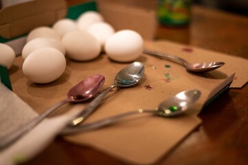 Closeup shot of spoons with coloring stains alongside fresh eggs on a brown surface