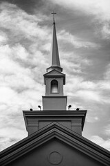 Low angle grayscale view of Christian chapel against cloudy sky background