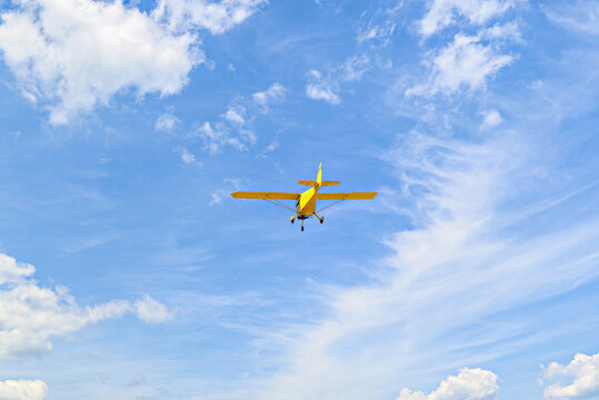 Yellow single-engine ultralight airplane flying in the blue sky with white clouds