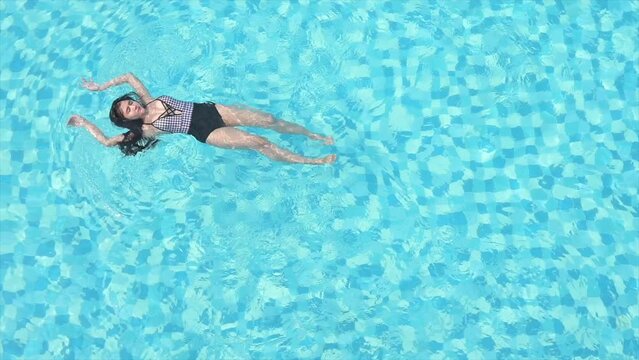 Aerial view of a woman swimming in a backstroke style in a pool on a hot summer day
