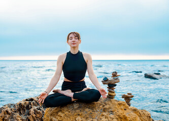 Fototapeta na wymiar young female is sitting in yoga lotus pose on the stone near the ocean
