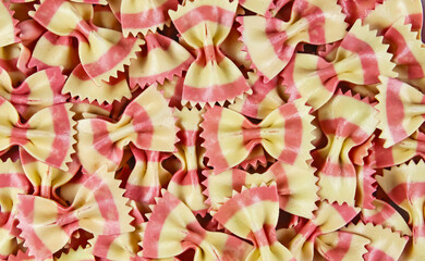 Full frame closeup of many bow tie butterfly shape pink yellow striped uncooked raw farfalle pasta...
