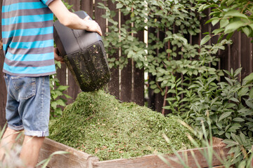 Gardener Throwing Grass from Lawn Mower into Compost Bin. Recycling Garden Waste Cutting Grass to...