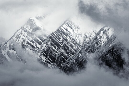 Grayscale of mountain peaks emerging in the fog in Conthey, Valais, Switzerland