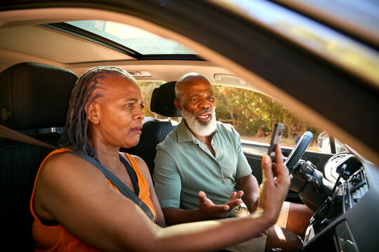 Senior Couple In Car Arguing About Directions On GPS Sat Nav On Mobile Phone On Day Trip Out