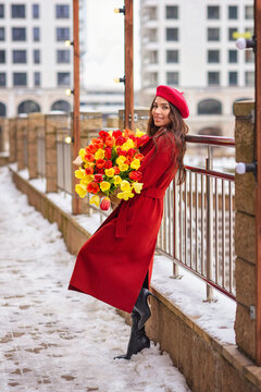 beautiful charming girl in the spring walks in the city in a red coat with flowers tulips. holiday girl