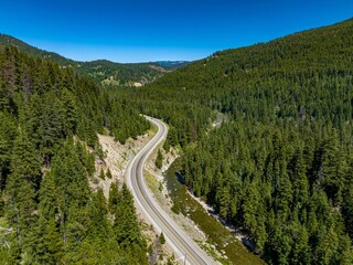 Drone view of Crowsnest Highway by river passing through rocks, dense forests and mountains, Canada.