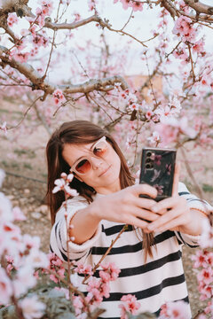 Vertical picture of attractive smiling woman taking a selfie in a cherry blossom field