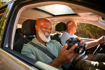 Passenger Taking Photo With Camera As Two Senior Male Friends Enjoy Day Trip Out In Car