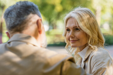 Smiling blonde woman looking at blurred husband in spring park.