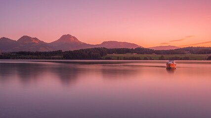 Boat in the water with lush trees and mountains in the background at sunset