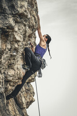 Beautiful black-haired woman with ponytail practicing climbing as a sport. Concept of extreme sports and risk. - obrazy, fototapety, plakaty
