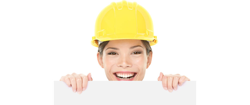 Construction worker engineer woman showing sign wearing yellow hard hat. Happy young woman holding peaking over white blank billboard card. Woman Isolated on transparent background in PNG cutout.