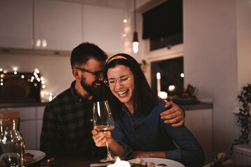 Couple laughing over glasses of wine during a candlelit dinner party