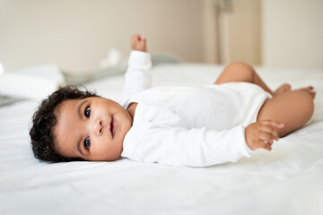 Cute little african american baby lies on bed, rest and relax, enjoy free time and good morning in...