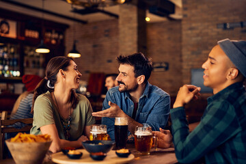Group of happy friends talk while drinking beer in bar.