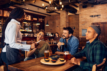 Fototapeta na wymiar Group of young people choosing order from digital menu while talking to waitress in pub.