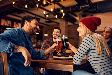 Young happy couple have fun while toasting with beer in pub.