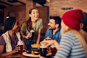 Young cheerful people drink beer and talk while gathering in pub.