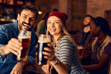 Happy couple raising a toast in pub and looking at camera.