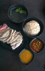 Hainanese chicken rice with soup and two sauces on dark wood table texture