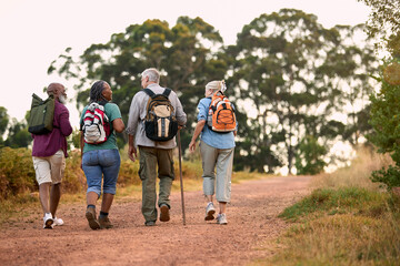 Rear View Of Active Senior Friends Enjoying Hiking Through Countryside Walking Along Track Together