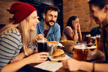 Group of young happy people drink beer and talk in pub.