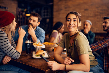 Young happy woman gathering with her friends in pub and looking at camera.