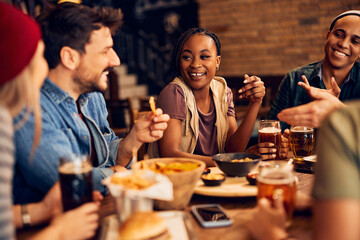 Happy black woman and her friends drink beer while talking in bar.