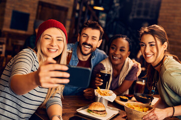 Group of cheerful friends have fun while taking selfie with mobile phone in pub.