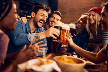 Multiracial group of happy friends has fun while toasting with beer in pub