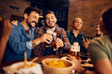 Happy men toasting while drinking beer with friends in bar.