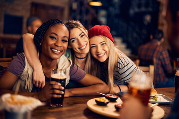 Young happy female friends in pub looking at camera.