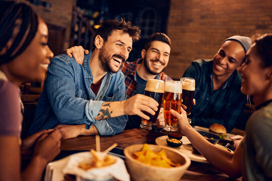 Cheerful man and his friends toast with beer while gathering in bar.