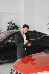 Good looking, cheerful and friendly indian salesman poses in a car salon or showroom.