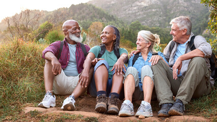 Active Senior Friends Sitting Taking A Break Hiking Through Countryside Together