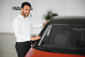 Indian man adult customer male buyer client wears classic suit white shirt chooses auto wants to buy new automobile touch check car in showroom vehicle salon dealership store motor show indoor.