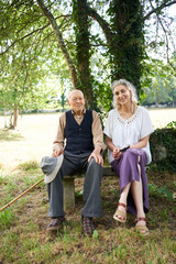 A ninety-six-year-old father rests seated on a stone bench next to his daughter, after a morning walk in the countryside. Two generations together relaxing and enjoying each other's company.