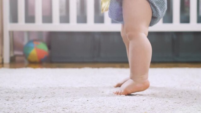 Baby learning to walk taking first steps at home. Little feet walking on floor at living room