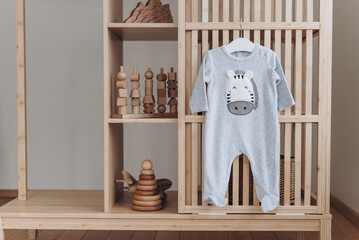 Baby bodysuit with zebra face on hanger, beige background. Cute children's clothes and wooden toys,...