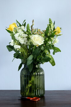 A green glass jar with a display of beautiful summer flowers, including white and yellow roses.