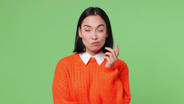 Excited smart young woman of Asian ethnicity wears orange sweater look around think scratches at temple comes up with idea raised finger get plan isolated on plain pastel light green color background