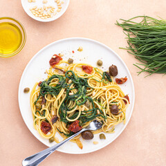Spaghetti  with Italian Agretti, Barba di frate or Saltwort or  Salsola Soda, olives, anchovy, tomatoes, capers,  pine nuts and olive oil, spring Italian recipes. Pink soft background, square crop
