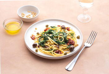 Spaghetti  with Italian Agretti, Barba di frate or Saltwort or  Salsola Soda, olives, anchovy, tomatoes, capers,  pine nuts and olive oil, spring Italian recipes. Pink soft spring background