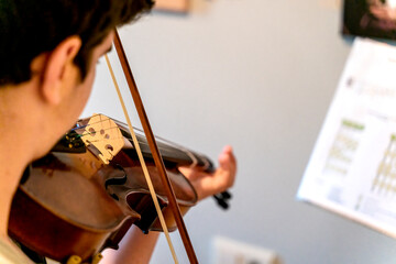 Detail of an unrecognizable young man practicing playing the viola or violin in his room with sheet music. Concept of people and music.