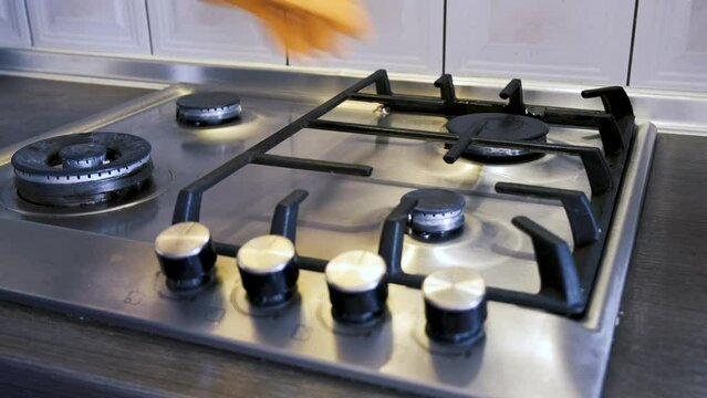 A man wearing protective gloves puts cast-iron grates on a stainless steel gas surface and wipes them clean of dirt with a kitchen sponge. Up close
